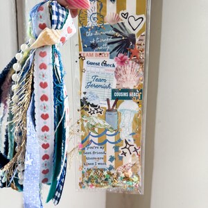 May include: A clear, rectangular shaker bookmark with a beach theme, featuring seashells, hearts, and the text "the summer & turned pretty". The bookmark has a blue and white gingham ribbon and a tassel with ribbons and beads.