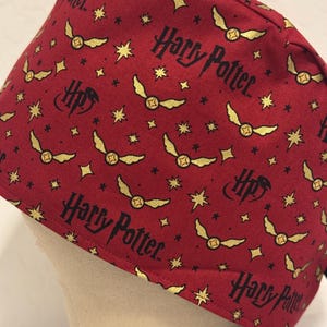 May include: Red scrub hat with a repeating pattern of gold snitches, stars, and the text "Harry Potter".