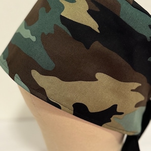 May include: A camouflage patterned surgical scrub hat with black ties. The hat is made of a soft, comfortable fabric and is designed to be worn during surgery or other medical procedures.