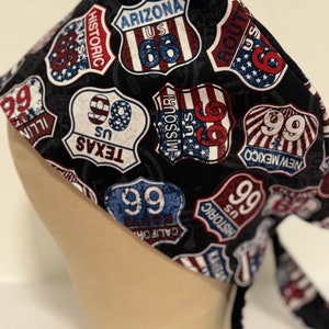 May include: A black fabric head wrap with a repeating pattern of red, white, and blue US Route 66 and 99 signs. The signs are in a shield shape with the text "US" and the route number.