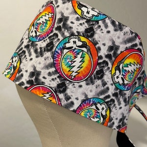 May include: A black and white tie-dye patterned surgical scrub hat with a repeating pattern of a skull and lightning bolt inside a circle.