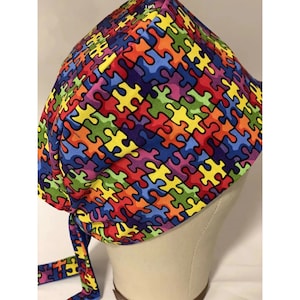 May include: A colorful surgical scrub hat with a puzzle piece pattern. The hat is tied with a long tie that matches the pattern.