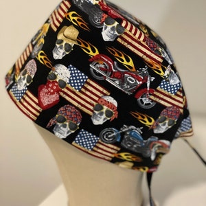 May include: A black surgical cap with a skull and motorcycle design. The cap features American flag patterns and flames.