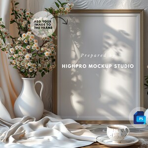 May include: A white frame mockup with a gold trim, sitting on a wooden table with a white pitcher and flowers, a cup and saucer, and a small plant in a white vase. The text "Prepared by HIGHPRO MOCKUP STUDIO" is visible at the bottom of the frame.