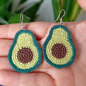 May include: A pair of crocheted avocado earrings with green and brown details. The earrings are hanging from silver hooks.