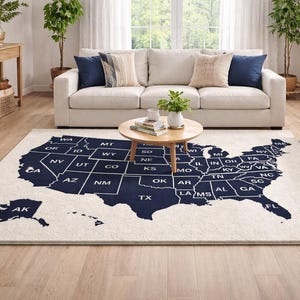 May include: A large, rectangular area rug with a map of the United States in navy blue against an off-white background. The rug features state outlines and abbreviations. The rug is placed in a living room with a sofa and coffee table.