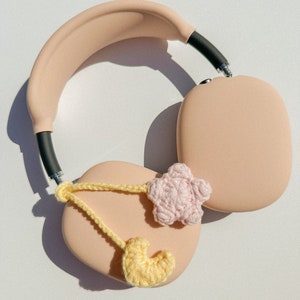 Pode incluir: Fones de ouvido circum-aurais cor de rosa claro com faixa de cabe&ccedil;a e conchas pretas. Os fones de ouvido s&atilde;o decorados com um cora&ccedil;&atilde;o de croch&ecirc; amarelo e uma estrela de croch&ecirc; rosa, conectados por uma corrente de croch&ecirc; amarela.