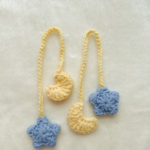 Pode incluir: Dois enfeites de croch&ecirc; feitos &agrave; m&atilde;o com um tema celestial. Um tem uma estrela azul clara e uma lua crescente amarela. O outro tem uma lua crescente amarela e uma estrela azul clara. Ambos t&ecirc;m um cord&atilde;o amarelo para pendurar.