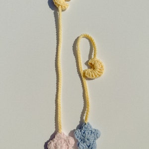 Pode incluir: Dois marcadores de croch&ecirc; feitos &agrave; m&atilde;o. Cada marcador apresenta uma forma de crescente amarelo no topo, conectado a um cord&atilde;o amarelo. Um cord&atilde;o termina com uma estrela rosa, o outro com uma estrela azul. O fundo &eacute; branco.