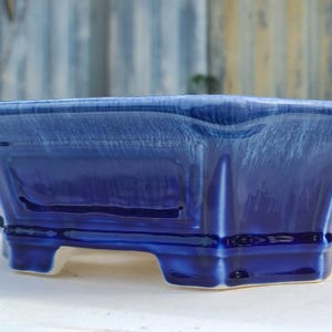 May include: A blue and white ceramic planter with a square shape and four legs. The planter has a glazed finish and a subtle ombre effect.