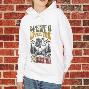 May include: White hoodie with a graphic of a skeleton hiking with a backpack and the text "Spent a little time on the mountain".