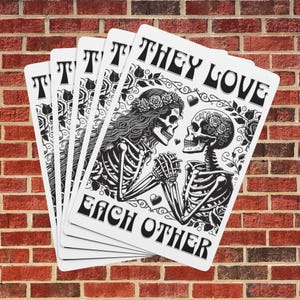 May include: A set of five white cards with black ink illustrations of two skeletons holding hands. The skeletons are wearing floral crowns and the text reads "They Love Each Other".