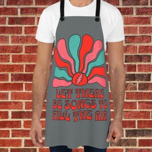 May include: Gray apron with a colorful graphic of a sun with the text "Let there be songs to fill the air".