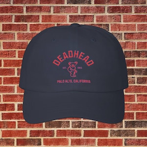May include: A navy blue baseball cap with red embroidered text that reads "Deadhead Est. 1965 Palo Alto, California" and a red embroidered bear graphic.