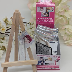 May include: A clear acrylic keychain featuring a colourful anime character image and the text "NO.KOI". The keychain is displayed on a small wooden easel. The keychain is part of a collection of acrylic keychains featuring characters from the anime "The Ancient Magus' Bride".