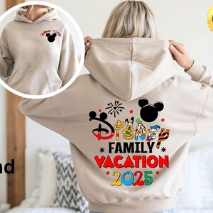Puede incluir: Una sudadera con capucha de color arena con un gran estampado gr&aacute;fico en la espalda. El gr&aacute;fico presenta a Mickey Mouse y otros personajes de Disney con el texto "Disney Family Vacation 2025".