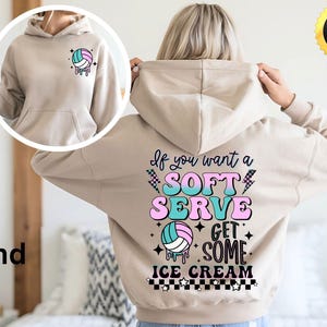 Könnte beinhalten: Ein beiger Hoodie mit einer Volleyballgrafik und dem Text "If you want a soft serve get some ice cream" in Rosa, Blau und Grün.