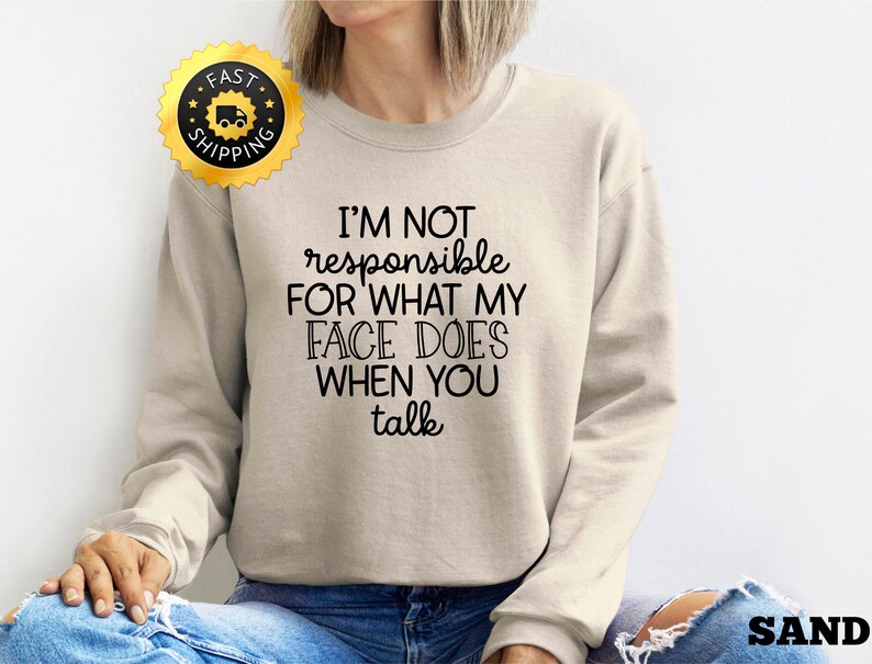 Puede incluir: Una sudadera beige con el texto "No soy responsable de lo que mi cara hace cuando hablas" impreso en negro.