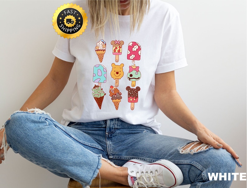 May include: White t-shirt with a colorful graphic of various ice cream pops featuring Disney characters like Winnie the Pooh, Mickey Mouse, and others.