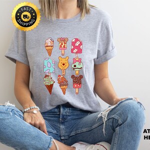 May include: A heather gray t-shirt with a graphic of various ice cream and popsicle designs featuring Disney characters like Mickey Mouse, Winnie the Pooh, and Stitch.