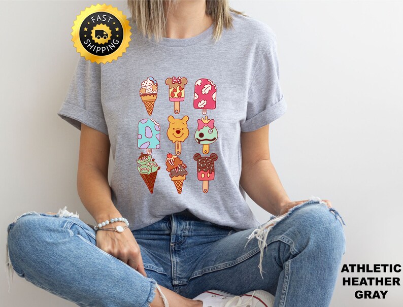 May include: A heather gray t-shirt with a graphic of various ice cream and popsicle designs featuring Disney characters like Mickey Mouse, Winnie the Pooh, and Stitch.