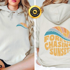 May include: A beige hoodie with a graphic of a sunset and waves on the back. The graphic says "Forever Chasing Sunsets".