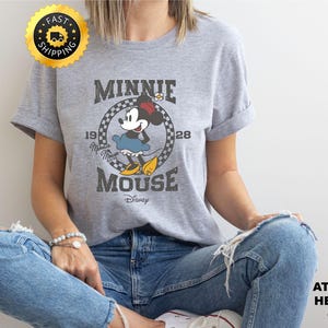 May include: Athletic heather gray t-shirt featuring a vintage Minnie Mouse graphic. The design includes the text "MINNIE MOUSE" and "1928". The shirt is a classic crew neck style.