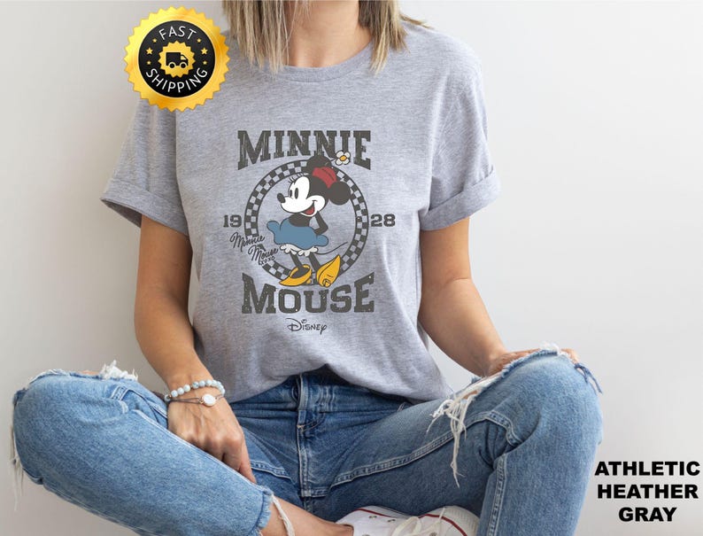 May include: Athletic heather gray t-shirt featuring a vintage Minnie Mouse graphic. The design includes the text "MINNIE MOUSE" and "1928". The shirt is a classic crew neck style.