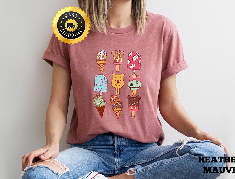 May include: A heather mauve t-shirt with a graphic of various ice cream and popsicle designs featuring Disney characters. The characters include Mickey Mouse, Minnie Mouse, Winnie the Pooh, and a green alien. The text "FAST SHIPPING" is on a gold star sticker in the top left corner of the image.