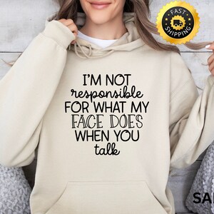 Puede incluir: Una sudadera con capucha beige con el texto "I'M NOT responsible FOR WHAT MY FACE DOES WHEN YOU talk" impreso en negro.