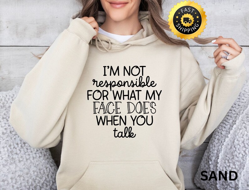 Puede incluir: Una sudadera con capucha beige con el texto "I'M NOT responsible FOR WHAT MY FACE DOES WHEN YOU talk" impreso en negro.
