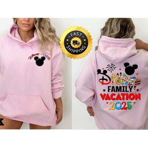 Puede incluir: Sudadera con capucha rosa con un gr&aacute;fico de Mickey Mouse en la parte delantera y un gr&aacute;fico de Disney Family Vacation 2025 en la parte trasera.