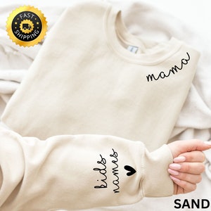 Könnte beinhalten: Ein beiger Pullover mit dem Wort "mama" auf der Vorderseite und den Worten "kids' room" und einem Herz auf dem linken Ärmel.