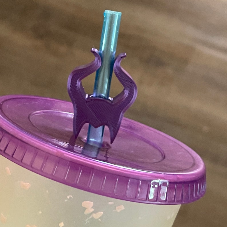 Pode incluir: Topper de palhinha de pl&aacute;stico roxo em forma dos chifres de Mal&eacute;vola da Bela Adormecida da Disney. O topper est&aacute; em cima de uma tampa roxa.