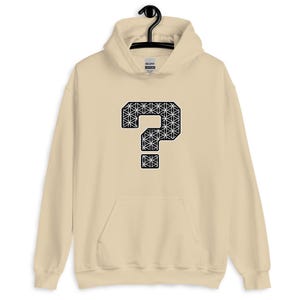 May include: A beige hooded sweatshirt featuring a large black and white question mark design on the front. The question mark is filled with a geometric pattern. The sweatshirt has a front pocket and a drawstring hood.