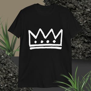 May include: Black t-shirt featuring a white crown design. The crown is a simple, hand-drawn style with three points and three small circles. The shirt is a short-sleeved crew neck.