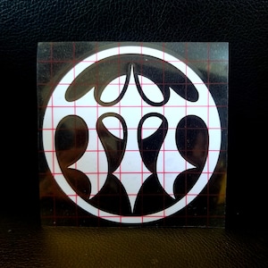 May include: A square sticker featuring a white circle with a black and white abstract design. The design consists of several curved, teardrop-shaped elements. The sticker is on a grid background.