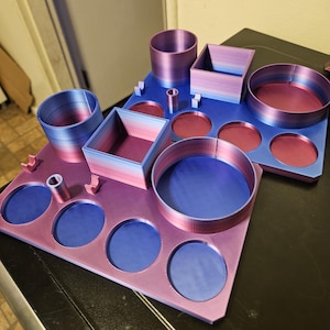 May include: Two 3D-printed desk organisers featuring a gradient colour scheme that transitions from blue to purple and pink. Each organiser includes various circular and square compartments, along with small U-shaped holders for pens or tools.