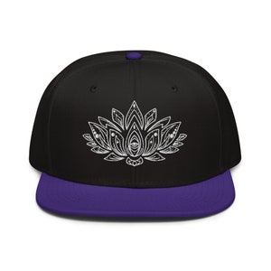 May include: A black and purple baseball cap with a white embroidered lotus flower design. The lotus flower has a detailed design with a central eye.