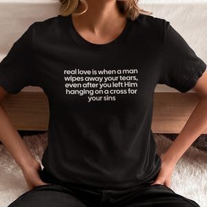 May include: Black t-shirt with white text: "real love is when a man wipes away your tears, even after you left Him hanging on a cross for your sins." The shirt is a crew neck style.