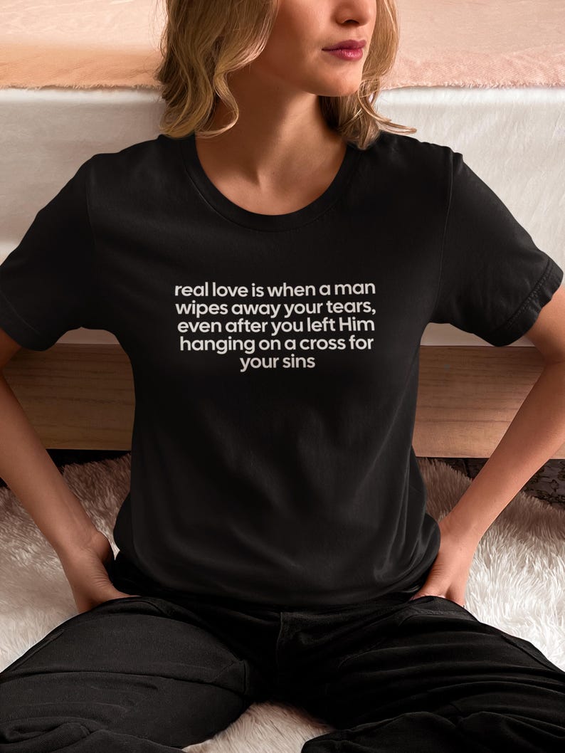 May include: Black t-shirt with white text: "real love is when a man wipes away your tears, even after you left Him hanging on a cross for your sins." The shirt is a crew neck style.