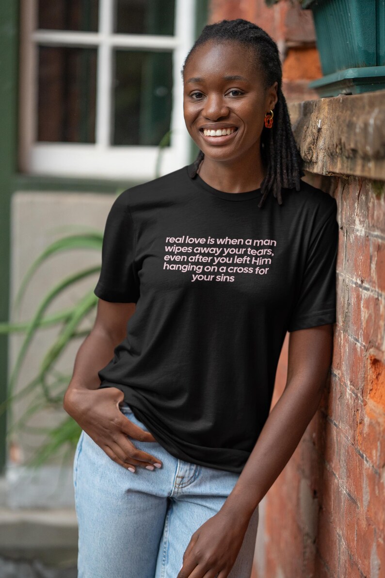 May include: Black t-shirt with the text "real love is when a man wipes away your tears, even after you left Him hanging on a cross for your sins" in pink. The shirt is worn by a person in light blue jeans.