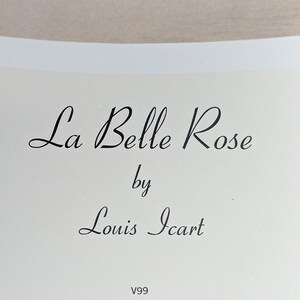 May include: Cream-colored print featuring the text "La Belle Rose" by Louis Icart in elegant black script. The artwork is set against a neutral background, with the letters in a flowing, cursive style. The print also includes the code "V99".
