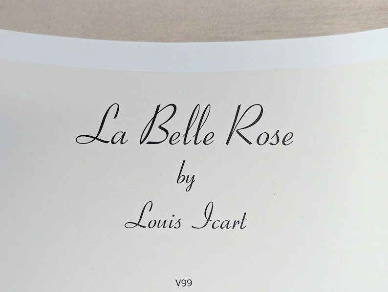 May include: Cream-colored print featuring the text "La Belle Rose" by Louis Icart in elegant black script. The artwork is set against a neutral background, with the letters in a flowing, cursive style. The print also includes the code "V99".
