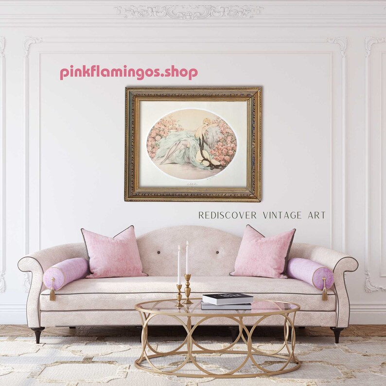 A staged interior scene featuring 'La Belle Rose' print by Icart framed and hung above a classic beige sofa with pink pillows.