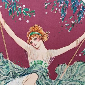 May include: Vintage art print of a woman on a swing. The woman has curly red hair, a green headband, and a flowing green dress. The background is a deep red with green foliage and white flowers.