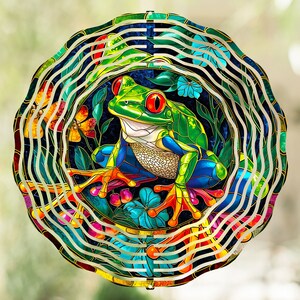 May include: A colorful metal wind spinner featuring a vibrant tree frog with red eyes, surrounded by flowers and butterflies. The frog is green, blue, and yellow, set against a dark background. The outer ring has a wavy, multi-colored design.