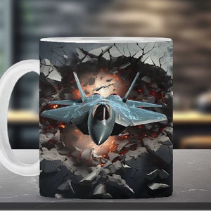 Könnte beinhalten: Eine weiße Keramiktasse mit einem Motiv eines Kampfjets, der eine Wand aus Beton und Feuer durchbricht.