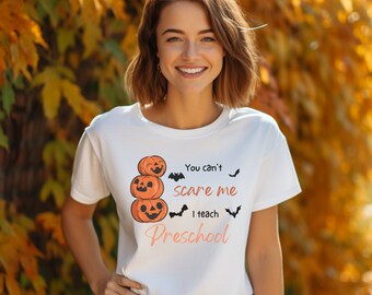 May include: White t-shirt with a graphic of stacked pumpkins and bats. The text reads "You can't scare me I teach Preschool".
