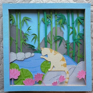 May include: A papercraft scene with a white cat sitting in a bamboo forest. The cat is looking down at a pond with lily pads and pink flowers. The background is a light blue sky with white clouds.